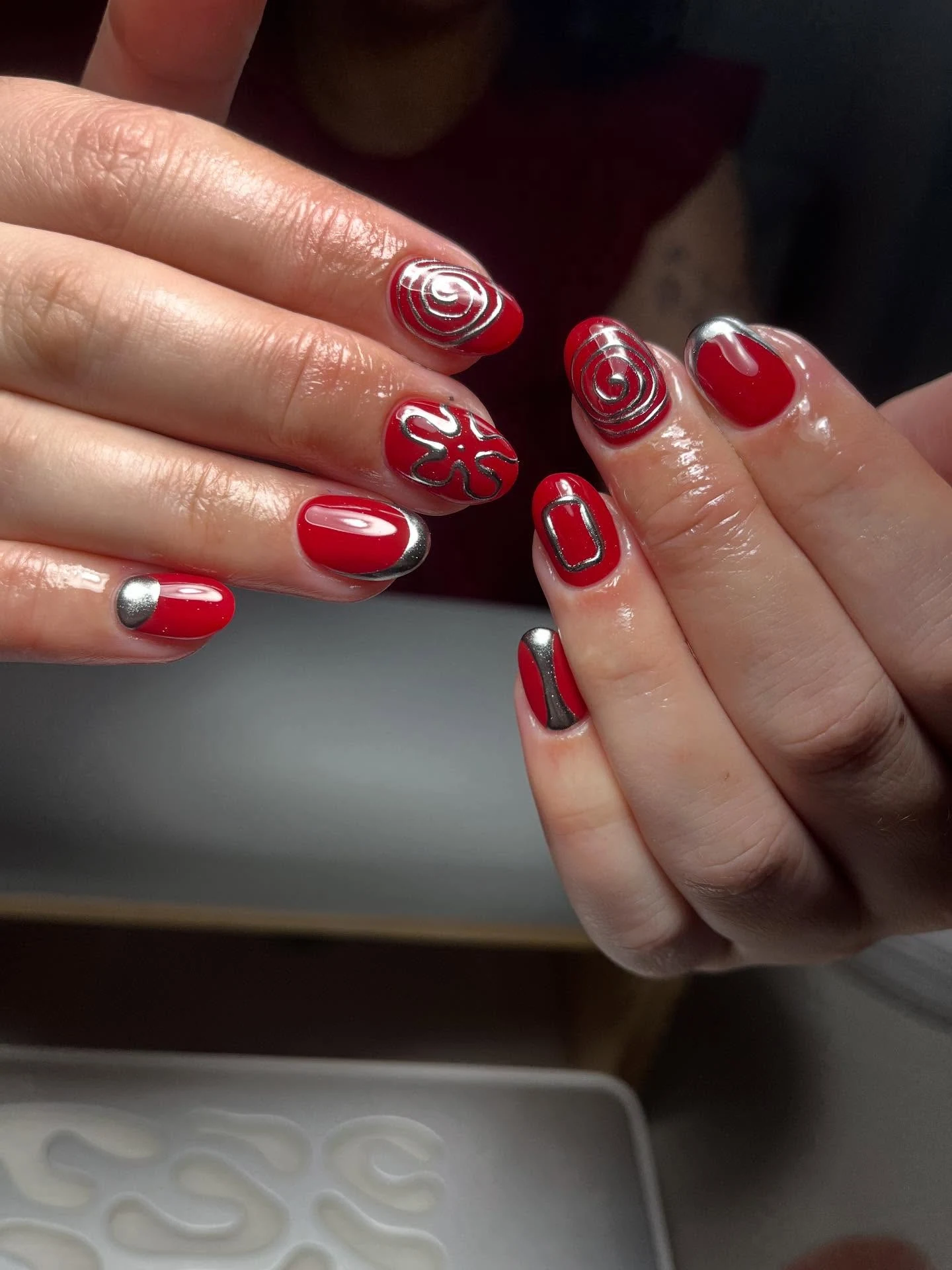 Bright red nails with silver hand-painted chrome spiral and line art