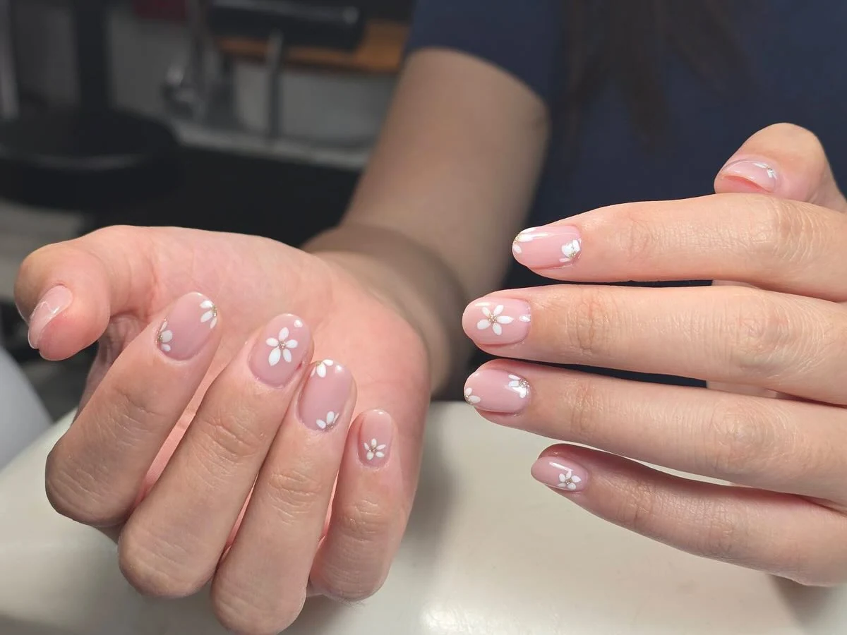 Soft nude nails with small white daisy flower art and gold-dot centres