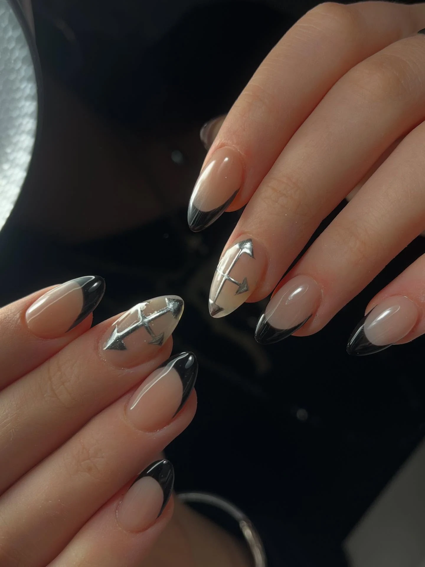Black French tips on nude almond nails with chrome arrow accents