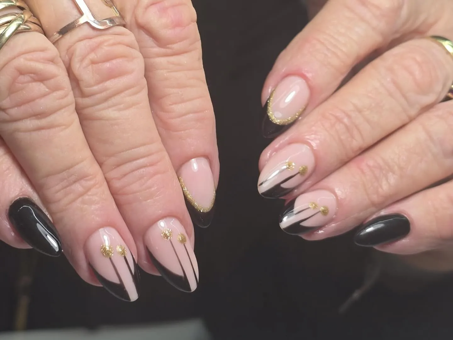 Black and gold negative-space almond nails with gold-dot accents and black-gold rings