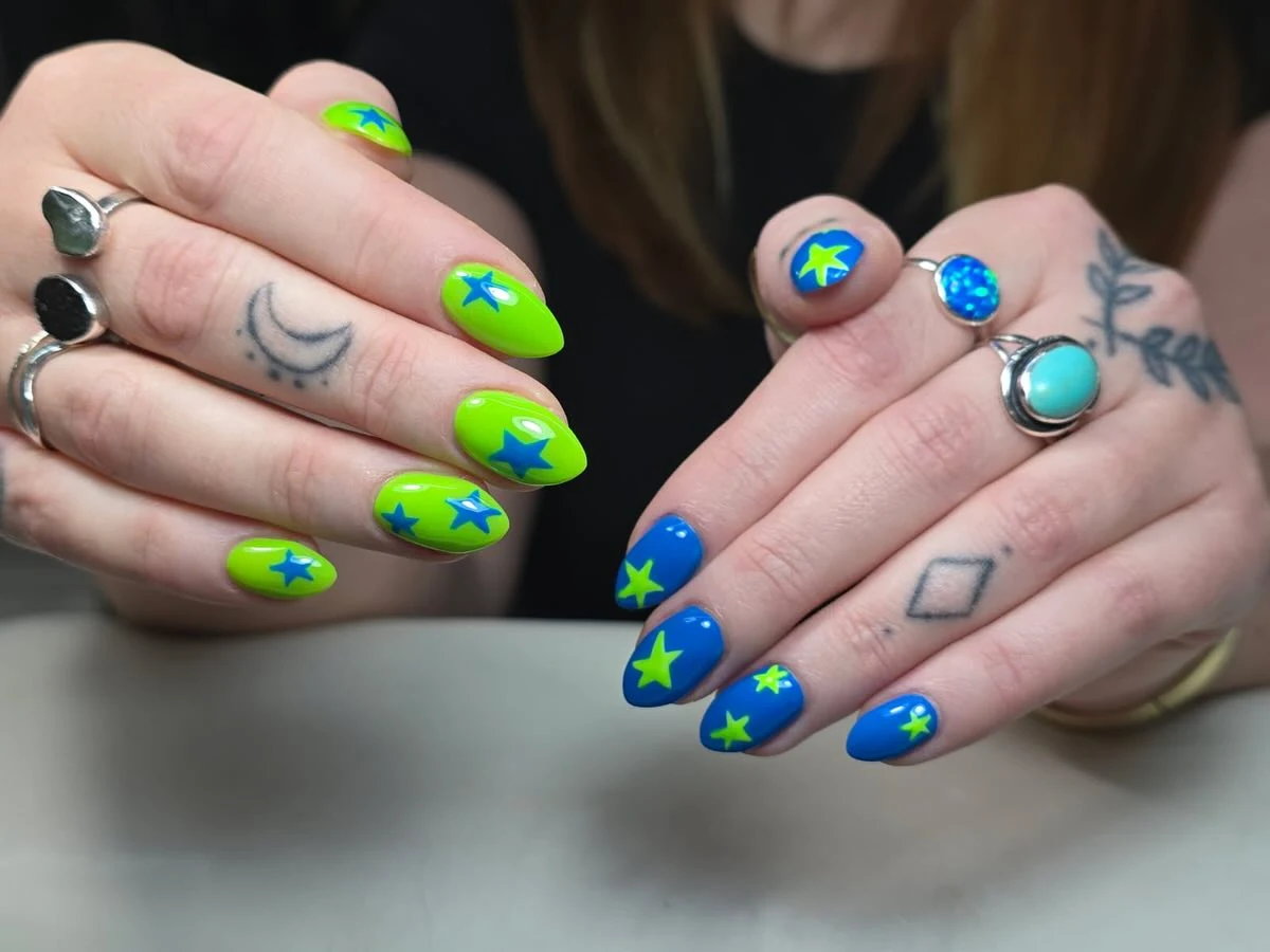 Neon lime-green and cobalt-blue nails with star accents and silver rings