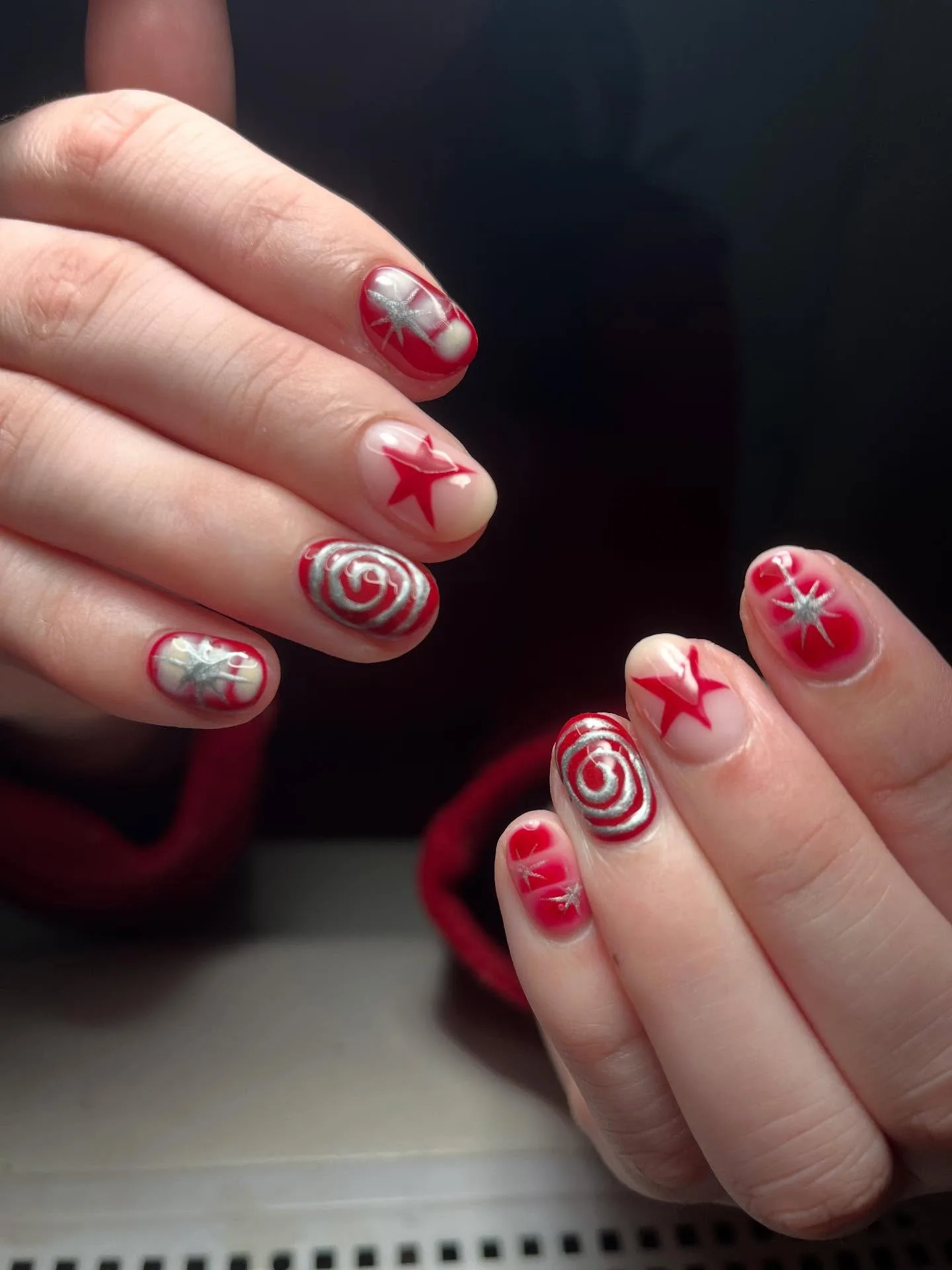 Bright red nails with silver star and spiral hand-painted art